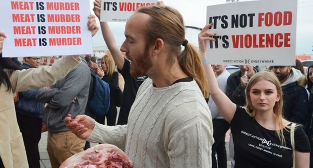 Hombre come cabeza de cerdo cruda frente a festival de vegetarianos