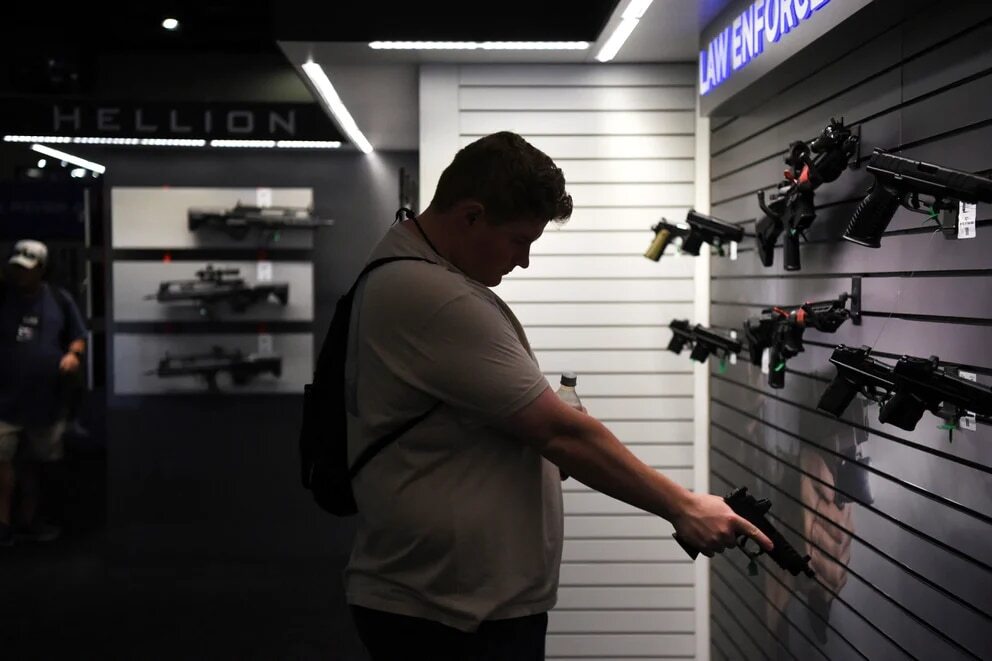 hombre sostiene una pistola en exhibicion en la convencion anual de la Asociacion Nacional del Rifle