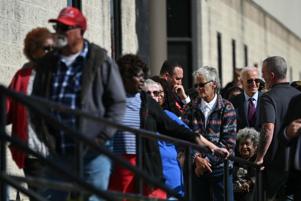 Biden hace fila para votar detras de un hombre con un sombrero profano a favor de Trump